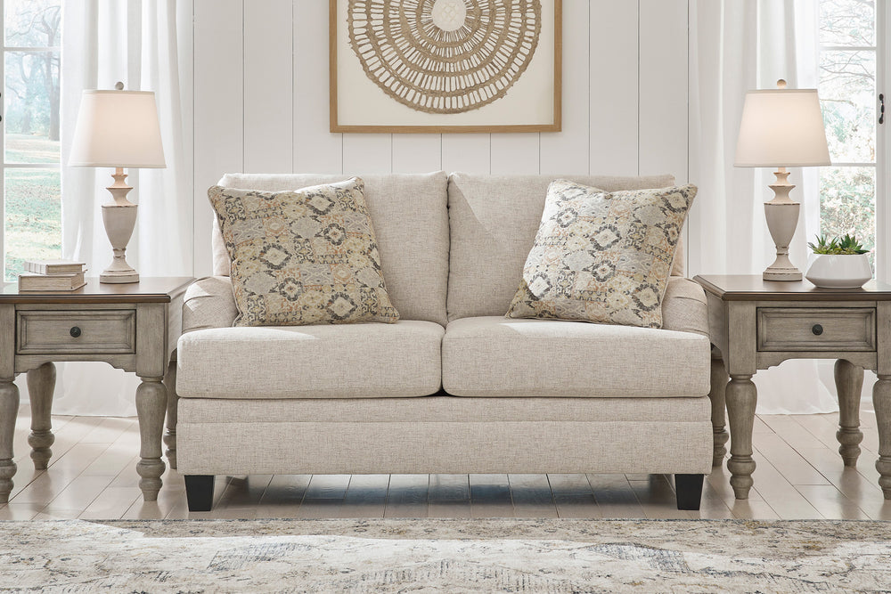 Loveseat beige con dos cojines decorativos y dos mesas de esquina a cada lado en un ambiente de sala. 
