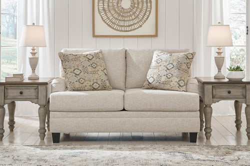 Loveseat beige con dos cojines decorativos y dos mesas de esquina a cada lado en un ambiente de sala. 