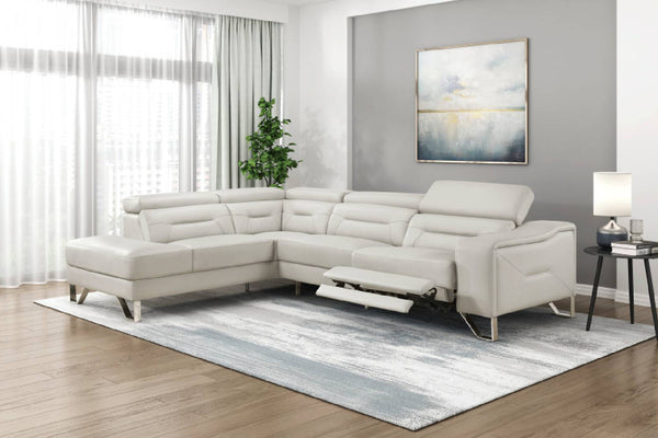 Un moderno sofá seccional de color beige claro con chaise longue y asiento reclinable, que se muestra en un ambiente de sala de estar ambientado con una pared gris, un cuadro abstracto, una mesa auxiliar y una alfombra estampada.