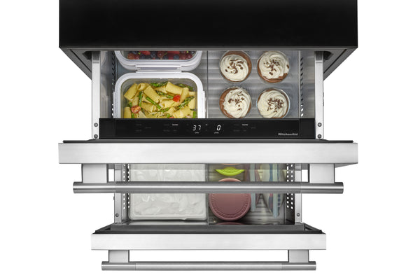 Una nevera de acero inoxidable de dos puertas verticales con ambos cajones inferiores abiertos, dejando ver los compartimentos para almacenar alimentos llenos de platos y recipientes.