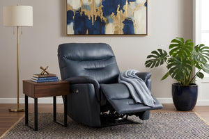 Sillón reclinable tapizado en color azul oscuro con respaldo alto acolchado, reposapiés extendido y apoyabrazos amplios. Ambientado en una sala moderna junto a una mesa auxiliar, lámpara de pie, planta decorativa y cuadro abstracto en tonos azul y dorado.