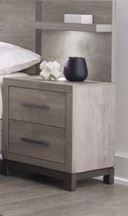 Una mesa de noche moderna de dos cajones con un acabado en veteado de madera gris claro y patas oscuras, mostrada en el entorno de un dormitorio junto a una cama. Esta pieza elegante aporta funcionalidad y un toque sofisticado a la habitación.