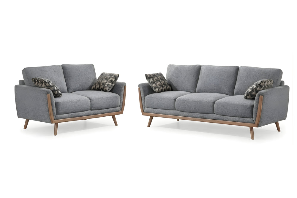 Conjunto de loveseat y sofá a juego, tapizados en tela gris y de estilo moderno de mediados de siglo, con estructura de madera clara y cojines decorativos estampados; se muestran sobre un fondo blanco.