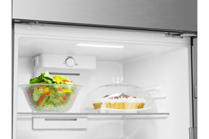 Puerta de una nevera abierta que muestra el estante interior blanco con un tazón de vidrio con ensalada a la izquierda y un postre cubierto a la derecha, todo situado frente a la puerta exterior de acero inoxidable sobre un fondo totalmente blanco.