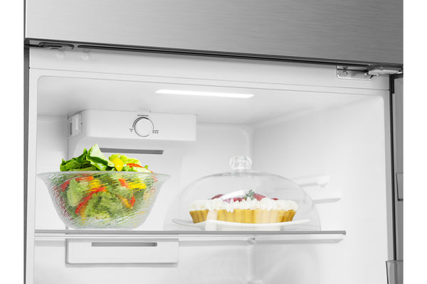Puerta de una nevera abierta que muestra el estante interior blanco con un tazón de vidrio con ensalada a la izquierda y un postre cubierto a la derecha, todo situado frente a la puerta exterior de acero inoxidable sobre un fondo totalmente blanco.