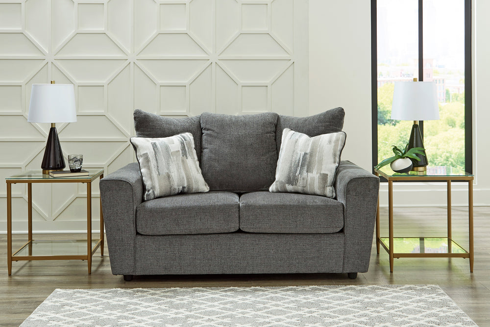 Loveseat gris con cojines decorativas sobre un fondo blanco. 