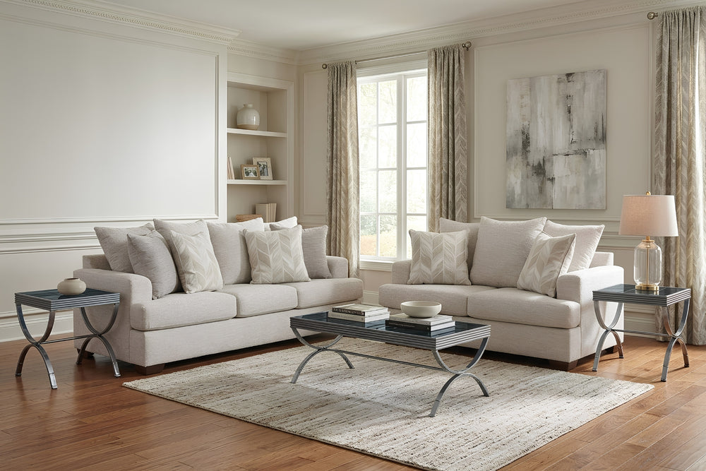 Juego de sala compuesto por sofá y loveseat tapizados en tela color beige claro, con cojines decorativos a juego y patas de madera oscura. Presentado sobre fondo blanco para resaltar el diseño contemporáneo y las líneas limpias del conjunto.