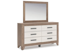 Un gavetero de seis gavetas con espejo rectangular a juego, que presenta un marco de madera de roble claro y frentes de cajón blancos con tiradores horizontales de color gris oscuro, mostrado sobre un fondo blanco.