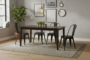 Mesa rectangular de madera marrón oscuro con cuatro sillas negras en un ambiente de sala. 