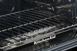 Primer plano del interior de un horno KitchenAid negro con una rejilla metálica y el logotipo de KitchenAid visible en el marco de la puerta del horno.