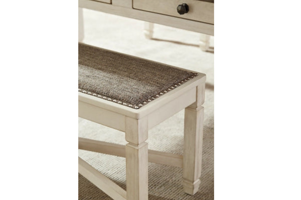 Primer plano de un banco de madera blanca con un cojín de asiento tejido de color marrón y detalles de tachuelas, mostrado en un ambiente de interior doméstico.