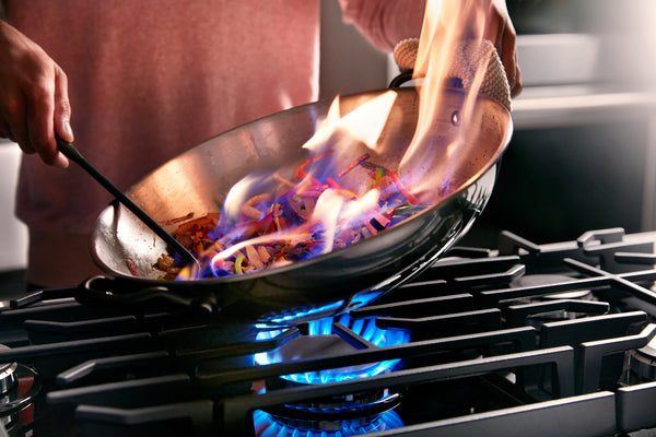 Persona cocinando en un wok sobre una estufa de gas con llamas.