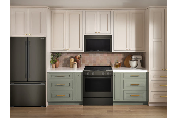 Un interior de cocina decorado que muestra armarios superiores de color crema, armarios inferiores de color verde salvia, una cocina independiente negra, un microondas negro, un refrigerador de acero inoxidable y un protector contra salpicaduras de azulejos rosas.