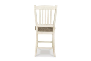 Una silla de comedor de madera individual, vista desde atrás, con una estructura pintada en color blanco roto con aspecto envejecido y un cojín de asiento tejido en color marrón texturizado, aislada sobre un fondo blanco.