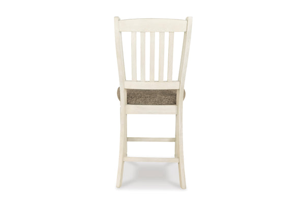 Una silla de comedor de madera individual, vista desde atrás, con una estructura pintada en color blanco roto con aspecto envejecido y un cojín de asiento tejido en color marrón texturizado, aislada sobre un fondo blanco.