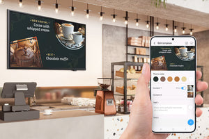 Persona que usa un teléfono inteligente para editar un menú digital  en un televisor en una cafetería.