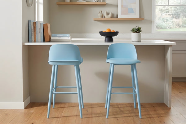 Dos taburetes azules frente a una encimera de cocina blanca, con una pared de color neutro y suelo de madera.