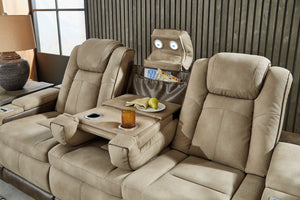 Sofá reclinable tipo home theater tapizado en tela beige, con consola central abatible, portavasos integrados, compartimiento organizador y luces de lectura incorporadas en los reposacabezas, ambientado en una sala moderna con lámpara lateral y panel decorativo de madera oscura.