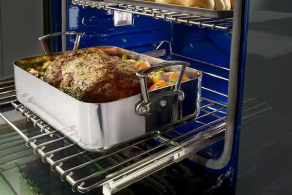 Primer plano del interior de un horno KitchenAid con acabado azul esmaltado. Muestra una bandeja para asar con carne y vegetales sobre una parrilla deslizante, diseñada para facilitar el acceso y la extracción segura de los alimentos.