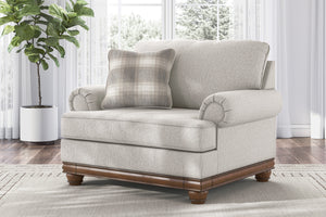 Silla de acento de color beige con brazos y un cojín decorativo en una sala con objetos decorativos. 