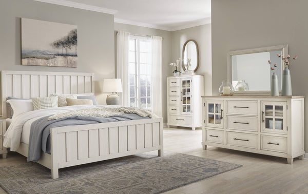 Conjunto de dormitorio antiguo de madera blanca que incluye una cama, un gavetero con espejo y un chest en una ambientación de habitación.