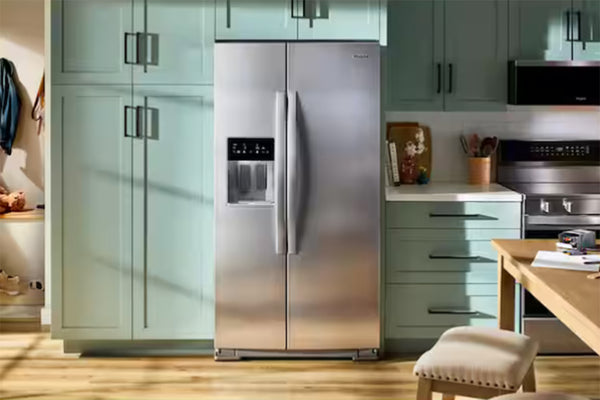 Refrigerador de acero inoxidable en una cocina moderna con gabinetes verdes y encimeras de madera.