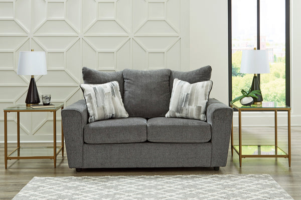Loveseat gris con cojines estampados en un ambiente de sala. 