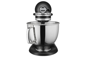 Una batidora KitchenAid con cabezal y base negros, y un gran bol de acero inoxidable con asa, mostrada sobre un fondo blanco liso.
