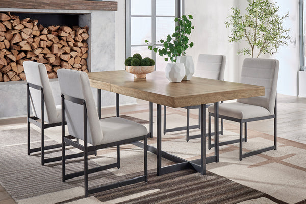 Comedor moderno con mesa rectangular de madera clara y estructura metálica negra, acompañado de cuatro sillas tapizadas en gris claro. Ambientado en un espacio luminoso con alfombra de diseño geométrico, plantas decorativas y chimenea con leña apilada.