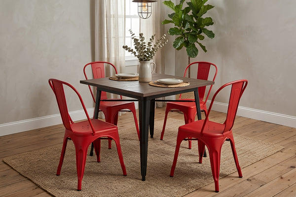 Mesa de comedor cuadrada con cubierta de madera oscura y estructura metálica negra, acompañada por cuatro sillas rojas de estilo industrial. El conjunto está sobre una alfombra tejida en un comedor moderno con planta decorativa y luz natural.