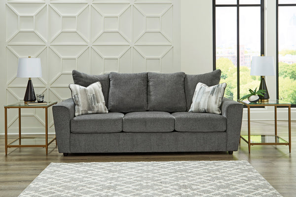 Sofá gris en sala con diseño geométrico de pared y grandes ventanales.