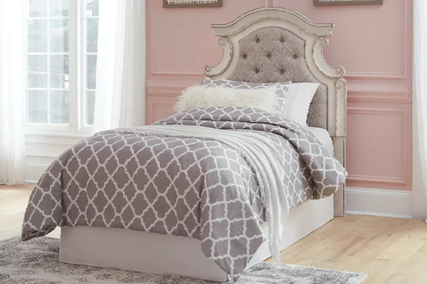 Cama color beige con capitoné y ropa de cama blanca en una habitación pintada de rosa.