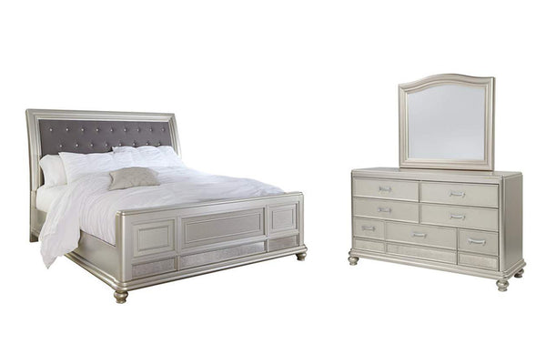 Conjunto de dormitorio plateado que incluye una cama capitoné gris con acolchado blanco y un gavetero con espejo sobre fondo blanco.