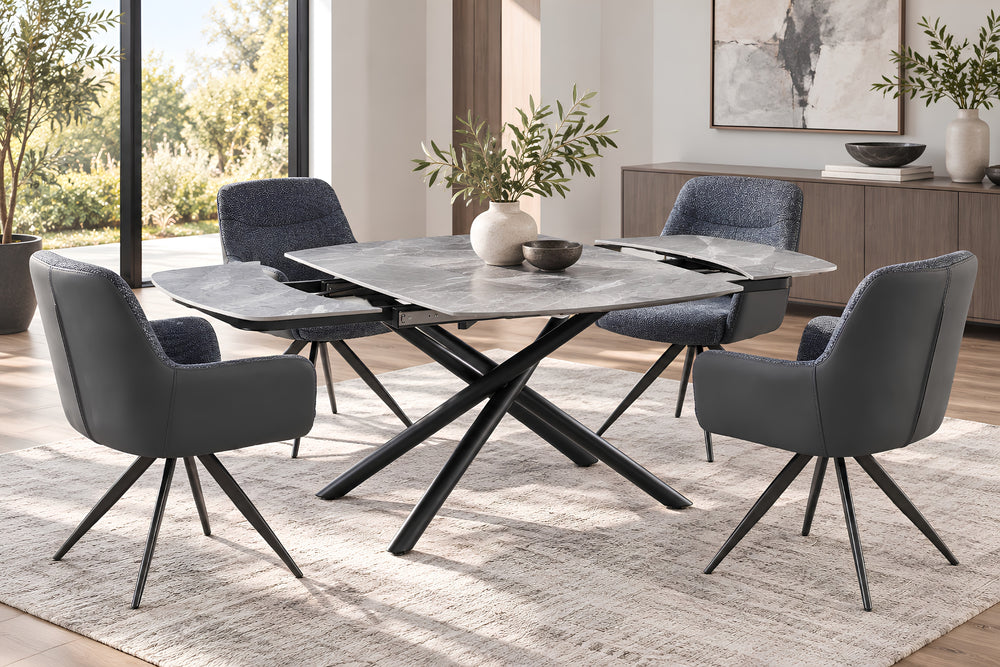 Juego de comedor moderno con mesa ovalada con tope gris y base en X negra, cuatro sillas tapizadas en gris con patas metálicas negras y una alfombra clara con textura en un comedor luminoso y contemporáneo