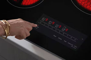 Mano presionando un botón en el panel de control de una estufa eléctrica con luces indicadoras rojas.