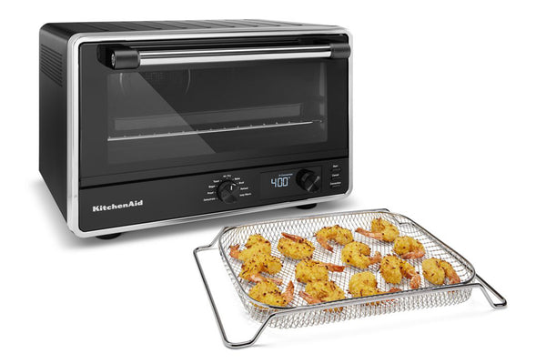 Horno de sobremesa KitchenAid en color negro y acero inoxidable, que se muestra con una cesta de alambre que contiene gambas fritas doradas sobre un fondo blanco.