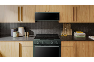 Una moderna cocina eléctrica verde y un microondas empotrado bajo armarios de madera de roble claro en un entorno de cocina.