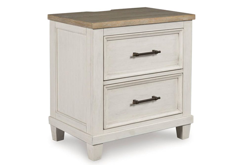 Vista lateral de una mesita de noche antigua de madera blanca con dos gavetas y tiradores negros sobre fondo blanco.