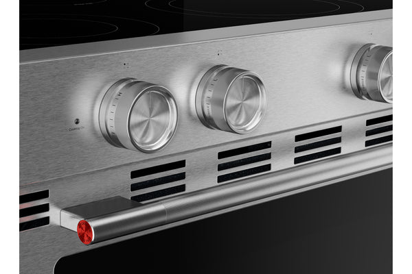 Primer plano del panel de control de un horno empotrado de acero inoxidable con tres perillas redondas plateadas, una manija horizontal con un detalle rojo y una placa de cocción de vidrio negro.