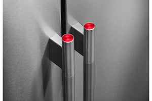 Primer plano de la puerta de una nevera moderno de acero inoxidable con dos tiradores cilíndricos con la parte superior de color rojo brillante, montados sobre un panel de puerta de metal cepillado a juego.