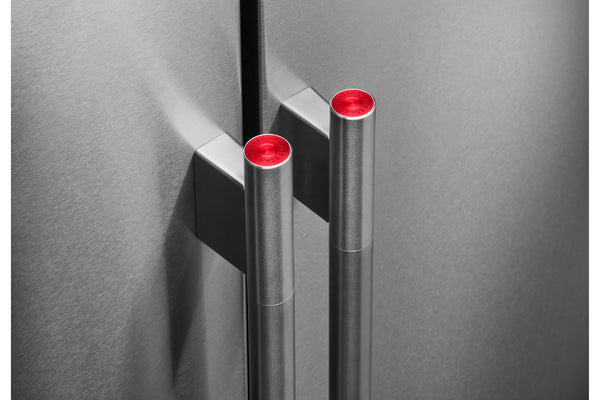 Primer plano de la puerta de una nevera moderno de acero inoxidable con dos tiradores cilíndricos con la parte superior de color rojo brillante, montados sobre un panel de puerta de metal cepillado a juego.