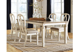 Juego de comedor de 5 piezas con mesa rectangular de madera gris desgastada y patas blancas vintage, 4 sillas a juego con asientos crema tapizados y respaldos curvos, sobre una alfombra de rayas en una habitación iluminada.