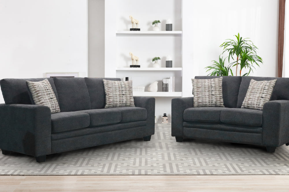 Sofá y loveseat de color negro con cojines decorativos sobre un fondo blanco. 