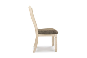 Vista lateral de una silla de comedor con estructura de madera pintada en color crema claro y cojín de asiento tapizado en color gris topo texturizado, sobre un fondo blanco liso.