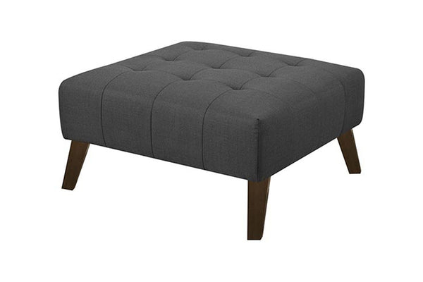 Ottoman tapizado de color gris y con patas acabadas en marrón sobre un fondo blanco. 