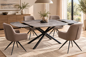 Una configuración de comedor moderno que presenta una mesa rectangular con acabado de piedra y base de metal negro en forma de X, rodeada por cuatro sillas tapizadas en color topo. El mobiliario se dispone sobre una alfombra beige texturizada en un comedor luminoso y contemporáneo, equipado con un aparador de madera, lámparas colgantes y grandes ventanales.
