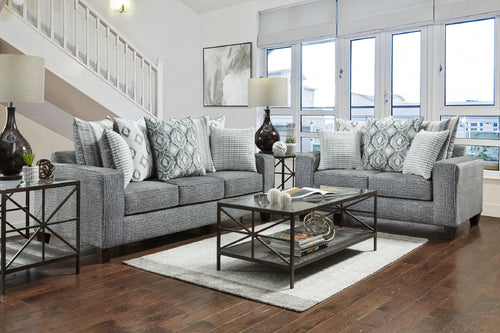 Sofá y loveseat de color gris con elementos decorativos en una sala de hogar con ventanas. 