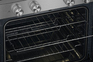 Primer plano del interior de un horno con dos rejillas metálicas dentro de una puerta de cristal oscuro, donde se aprecia parte de un panel de control de acero inoxidable y perillas plateadas en la parte superior.