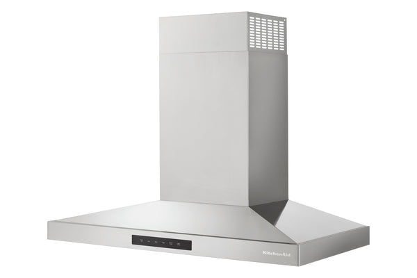 Una campana extractora de acero inoxidable con chimenea alta y base ancha con brida, mostrada sobre un fondo blanco liso. La marca «KitchenAid» es visible en el embellecedor frontal inferior derecho.