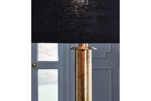 Lámpara decorativa con pantalla negra y base de latón sobre fondo neutro.